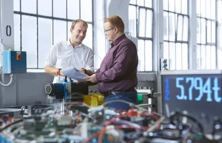 Zwei Mitarbeiter von Demag stehen in der Fertigung und beratschlagen über ein Projekt.